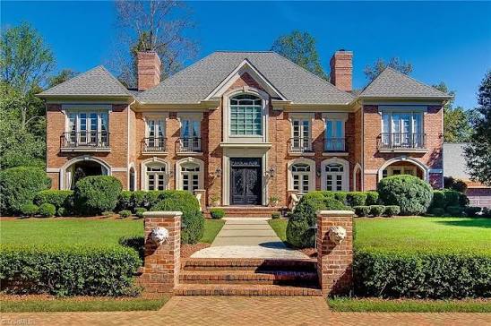 Two-story brick manor home with arched windows, balconies and a manicured front lawn